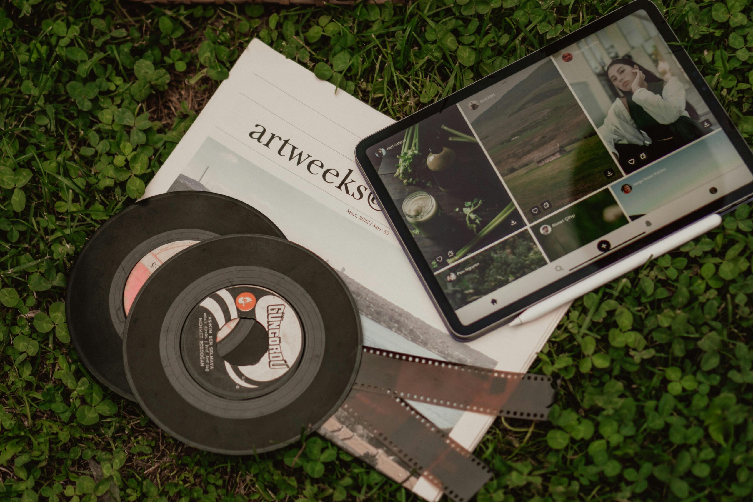 A flat lay of vintage films, a newspaper, and a tablet on grass.